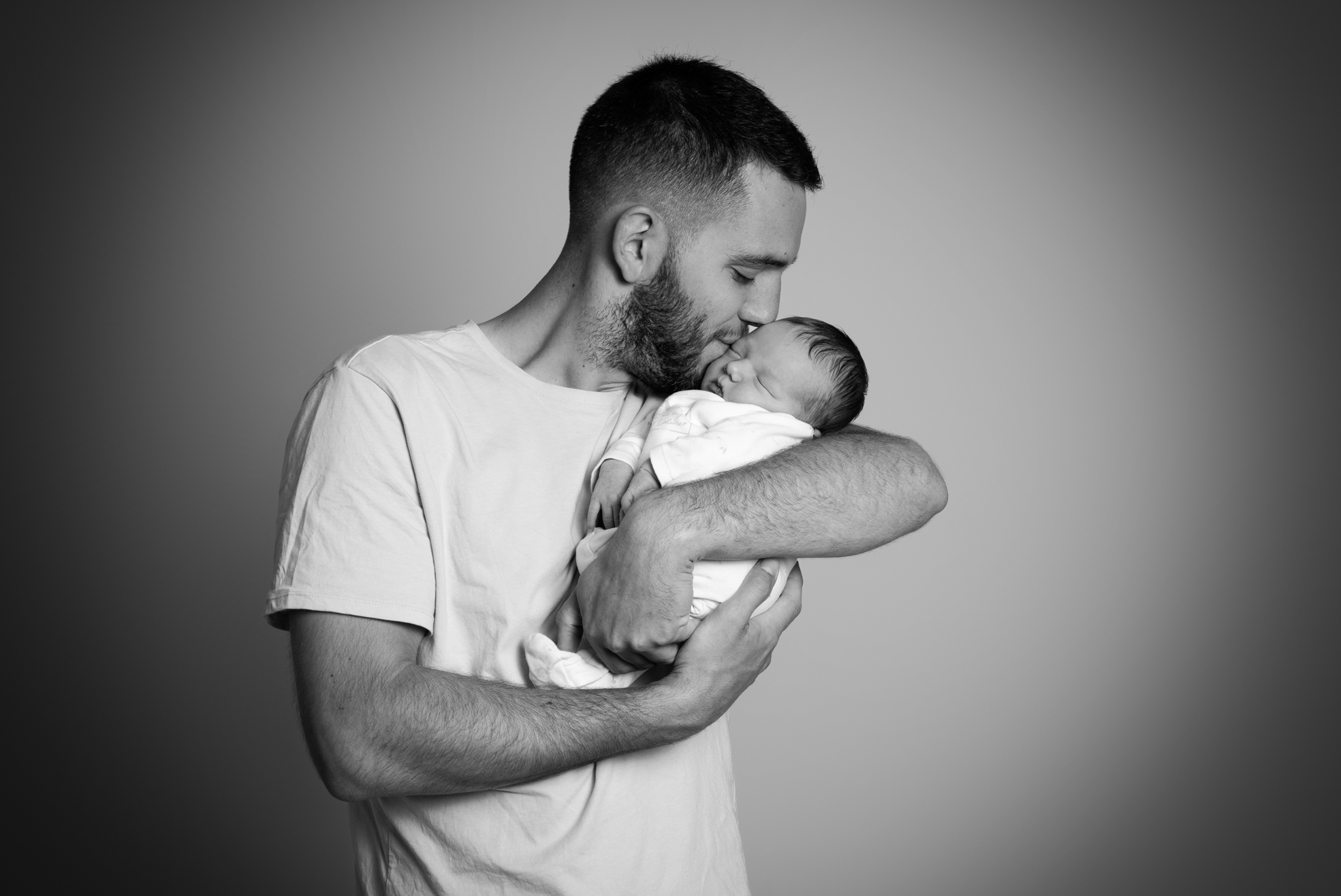 Papa faisant un petit bisou à son nouveau-né lors d’une séance naissance en studio à Bressuire.