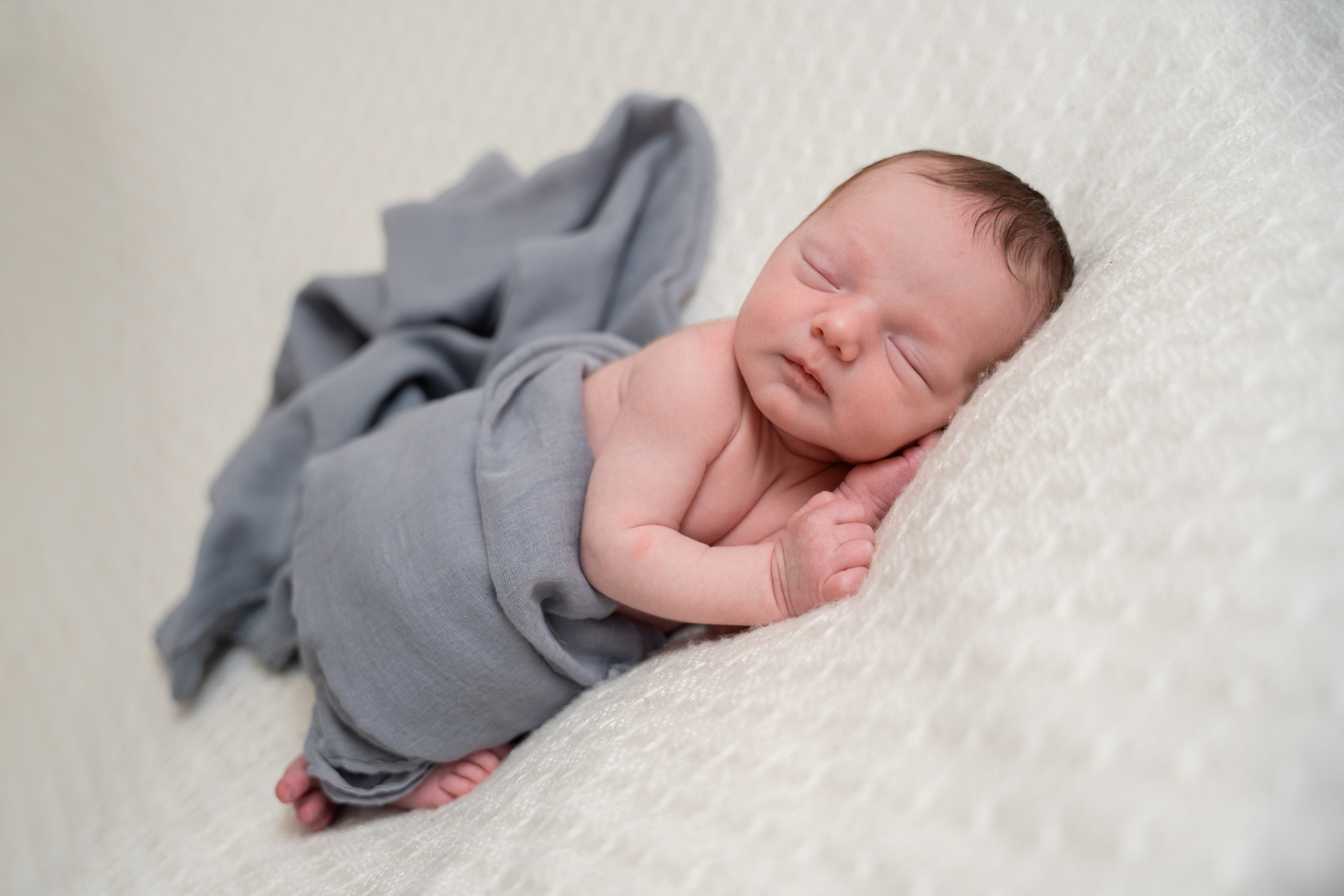 Nouveau-né endormi sur le côté, enveloppé dans une couverture douce.