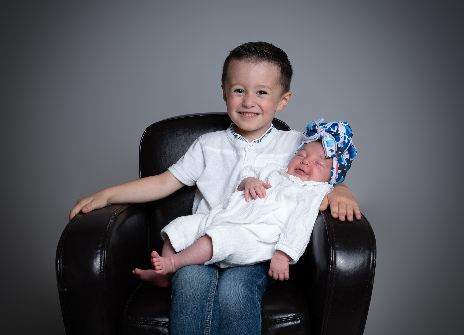 Aîné tenant délicatement son nouveau-né dans les bras lors d’une séance photo en studio.