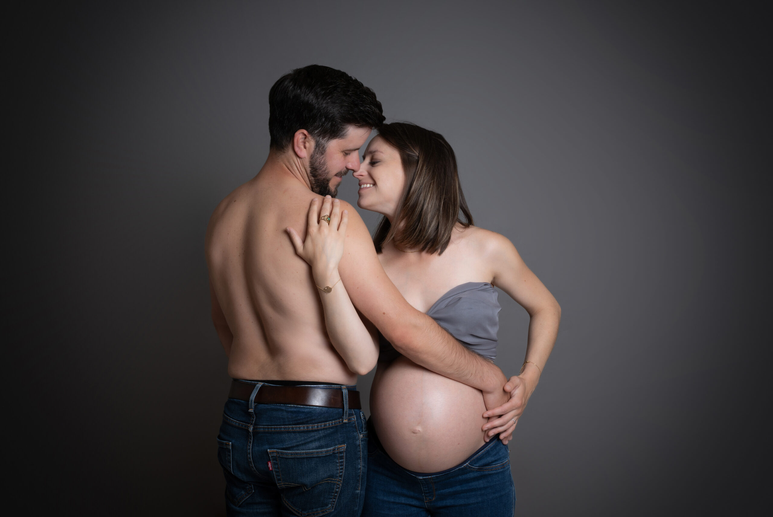 Couple tendre lors d’une séance photo grossesse en studio, la future maman dévoile son ventre arrondi