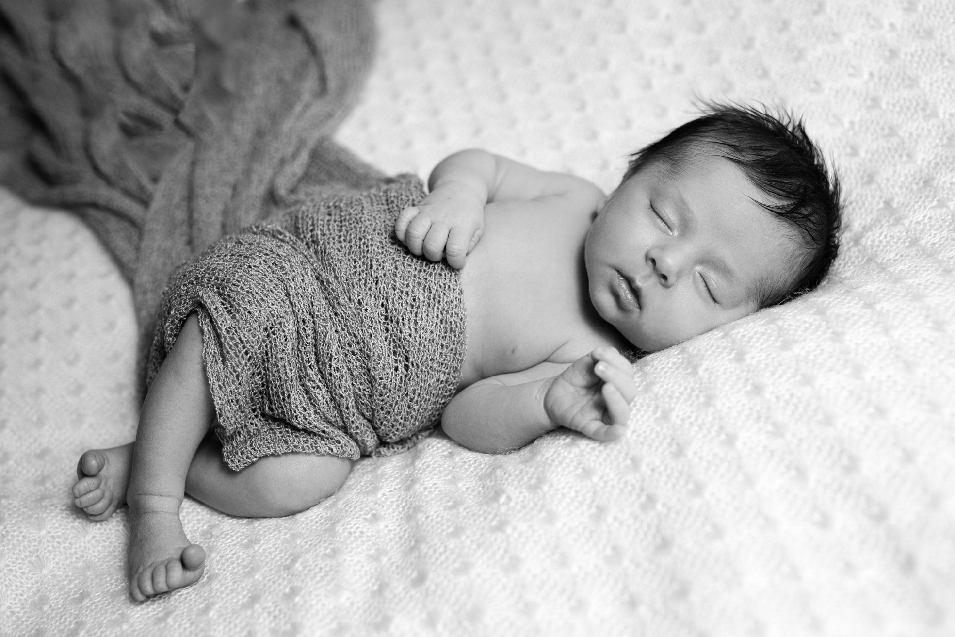 Nouveau-né photographié seul, enveloppé dans un tissu doux en studio.