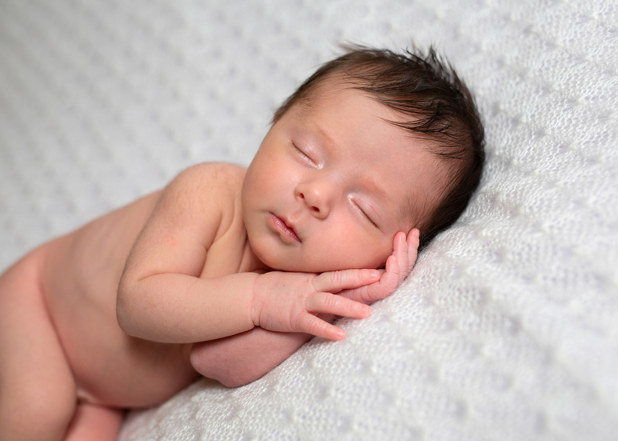 Nouveau-né assis légèrement soutenu sur un coussin en studio à Bressuire.