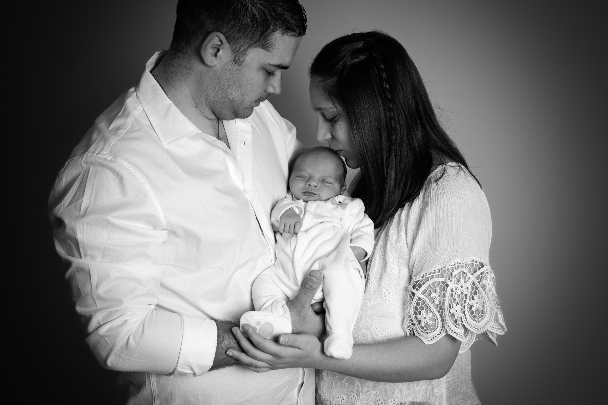 Nouveau-né dans les bras de ses parents lors d’une séance photo en studio.