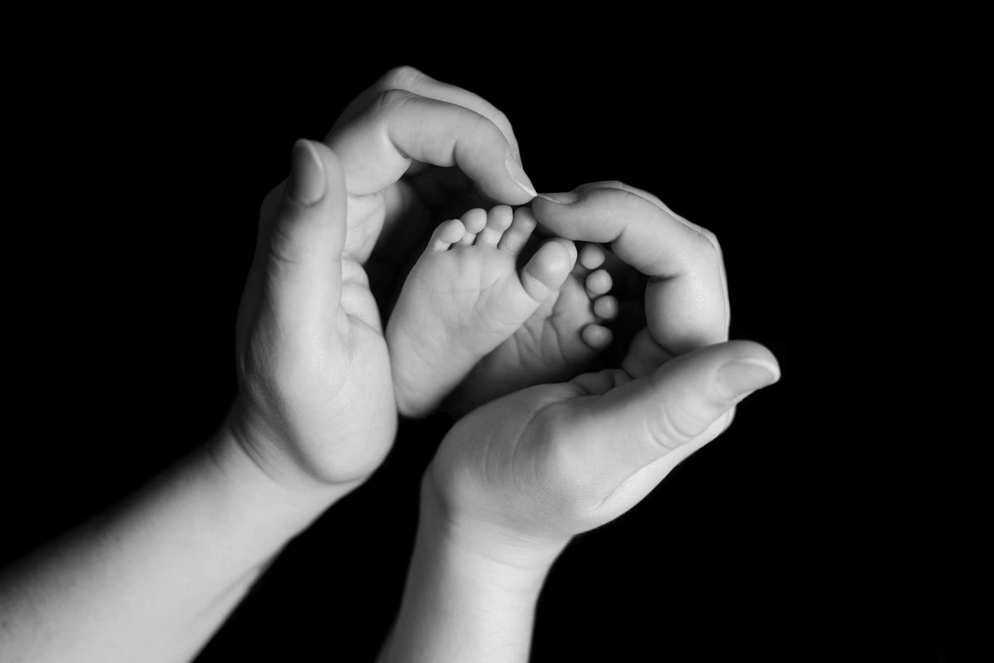 Mains de la maman entourant les petits pieds de son bébé lors d’une séance naissance en studio à Bressuire.