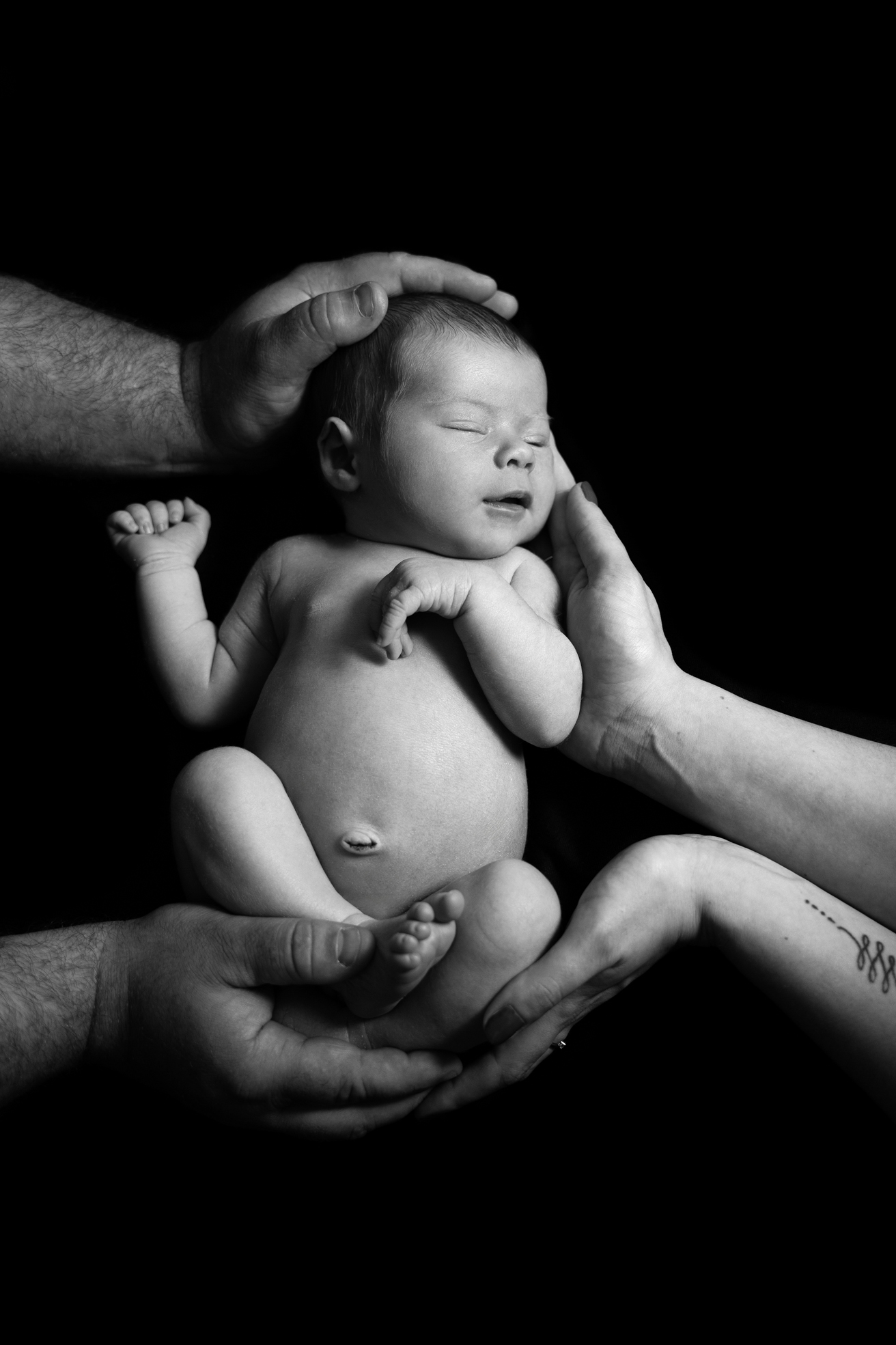 Nouveau-né tenu délicatement par les mains de papa et maman en studio à Bressuire.