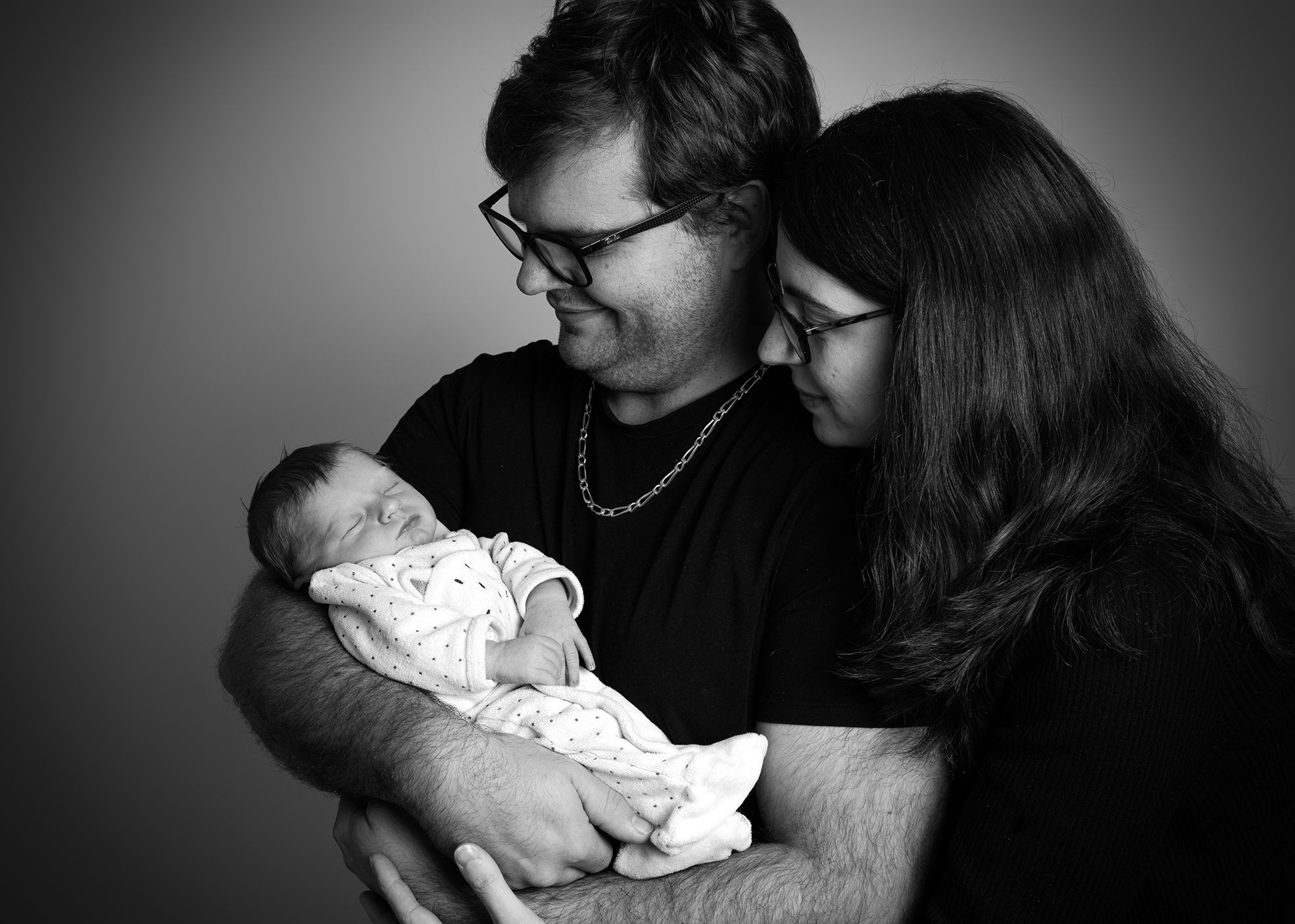 Nouveau-né dans les bras des parents, moment tendre et familial en studio.